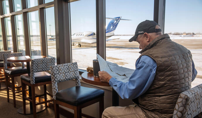 Man sitting at table reading newspaper by windows looking out to the runway